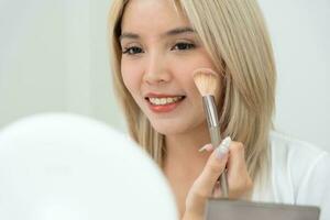 magnifique asiatique femme asseoir dans de face de une miroir. visage de une en bonne santé femme appliquant se maquiller. publicité pour peau se soucier, anti-rides, bébé affronter, blanchiment, Crème hydratante, serrer les pores sérum photo