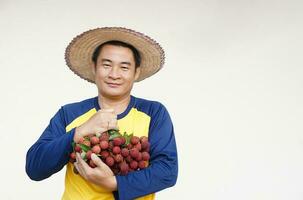 Beau asiatique homme agriculteur porte chapeau, Jaune chemise, détient litchi des fruits. concept, agriculture profession. thaïlandais Les agriculteurs grandir biologique litchis comme un exportation produit de Thaïlande. photo