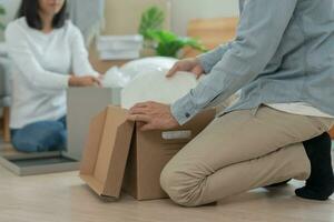 en mouvement loger, déménagement. couple Aidez-moi ensemble et bouge toi meubles pour Nouveau appartement, à l'intérieur le pièce a été une papier carton boîte contenir personnel affaires. bouge toi dans le Nouveau appartement ou condominium photo