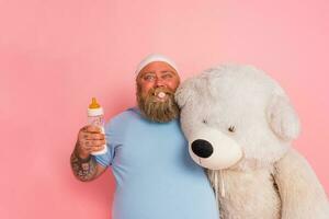 graisse homme actes comme une enfant avec sucette, bébé bouteille et une gros ours en peluche photo