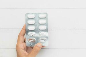 main en portant une cloque pack de médicament pilule sur blanc table Contexte pour médical et soins de santé concept photo