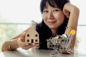 sélectif concentrer de asiatique femme main en portant une en bois maison modèle avec plein de pièces de monnaie dans achats Chariot photo