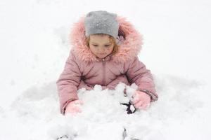 petite fille est assise dans la neige, jouant avec la neige fraîche qui est tombée pendant la nuit