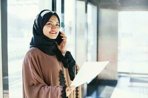 Jeune musulman femme dans hijab parlant sur téléphone et en portant papier photo