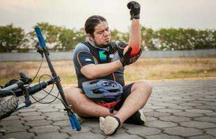 accidenté cycliste avec coude douleur. accidenté cycliste homme sur le chaussée dans douleur frottement le sien coude photo