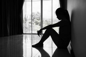 silhouette de déprimé Jeune femme près fenêtre à maison, fermer dans le foncé chambre. national violence, la violence contre femmenoir et blanc photo. photo