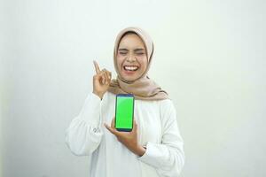excité magnifique asiatique musulman femme montrant vert écran mobile téléphone isolé plus de blanc Contexte photo