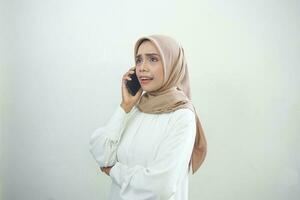 magnifique surpris asiatique musulman femme portant hijab en utilisant une mobile téléphone, dactylographie SMS message isolé sur blanc Contexte studio portrait. gens religieux mode de vie concept photo