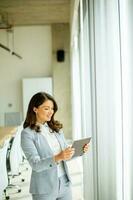 Jeune femme travail sur numérique tablette par le Bureau fenêtre photo