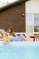 Jeune couple relaxant par le nager bassin dans le maison arrière-cour photo