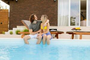 Jeune couple relaxant par le nager bassin dans le maison arrière-cour photo