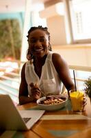 Jeune noir femme ayant une en bonne santé petit déjeuner tandis que travail sur portable dans le café photo