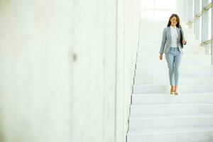 Jeune affaires femme en marchant vers le bas le escaliers et en portant portable photo