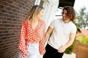 souriant Jeune couple dans l'amour en marchant dans de face de maison brique mur photo