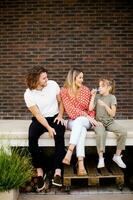 famille avec une mère, père et fille séance à l'extérieur sur le pas de une de face porche de une brique maison photo