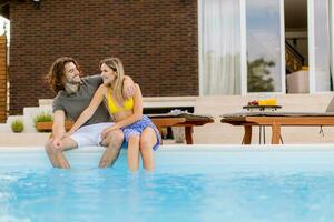 Jeune couple relaxant par le nager bassin dans le maison arrière-cour photo