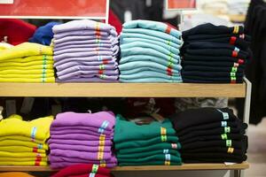 là sont piles de tricoté chandails, plié manches longues ou t-shirts sur une boutique étagère. vente vêtements dans une magasin. photo