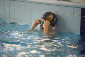 garçon dans une nager casquette et nager des lunettes de protection dans le bassin. le enfant est engagé dans le nager section. photo