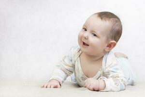 enfant avec une sourire sur une blanc Contexte. un adorable six mois vieux bébé garçon est mensonge sur le lit. conceptuel photo de paternité et maternité.