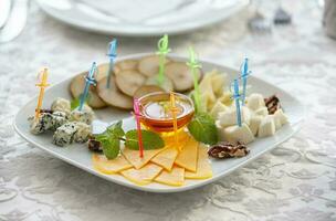 sur le assiette est un apéritif de tranché fromage de différent variétés, décoré avec brochettes. une plat pour une buffet tableau. photo