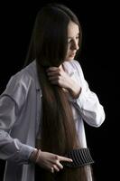 une magnifique brunette fille peignes sa longue lisse cheveux sur une foncé Contexte. photo