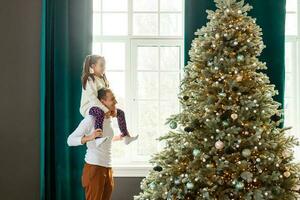 content père et le sien peu fille décorer le Noël arbre à maison. photo