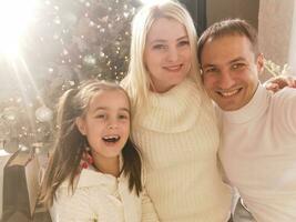 famille, vacances, La technologie et gens - souriant mère, père et peu fille fabrication selfie avec caméra plus de vivant pièce et Noël arbre Contexte photo