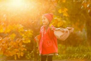 élève de primaire école avec livre dans main. fille avec sac à dos près bâtiment en plein air. début de cours. premier journée de automne. photo
