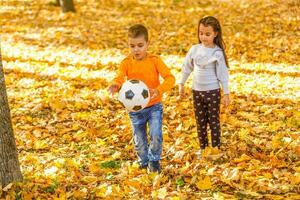 de peu garçon avec une Balle en jouant footballistique dans le l'automne parc photo