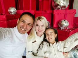 famille, vacances, La technologie et gens - souriant mère, père et peu fille fabrication selfie avec caméra plus de vivant pièce et Noël arbre Contexte photo