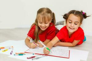 famille, loisir et enfance concept - content sœurs mensonge sur sol et dessin et Faire devoirs à Accueil photo