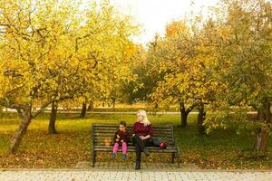 content mère et fille embrassement sur une banc dans un l'automne parc photo