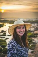 femme avec chapeau prendre plaisir le le coucher du soleil à le rocheux plage dans Gaïa, Porto, le Portugal. juni 17 2023. photo