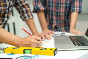 l'ingénieur asiatique et l'équipe partenaire apprennent et parlent avec le plan de projet de plan de maison, le graphique et le casque jaune et les outils de construction d'ingénierie sur le travail de table. photo