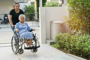 soignant Aidez-moi et se soucier asiatique personnes âgées femme patient séance sur fauteuil roulant à rampe dans allaitement hôpital, en bonne santé fort médical concept. photo