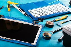 l'assistant répare l'ordinateur portable avec des outils et des mains sur la table en bois bleue. vue de dessus photo