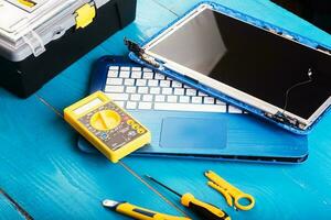 l'assistant répare l'ordinateur portable avec des outils et des mains sur la table en bois bleue. vue de dessus photo