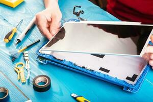 l'assistant répare l'ordinateur portable avec des outils et des mains sur la table en bois bleue. vue de dessus photo