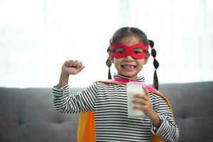 asiatique peu fille dans une super-héros costume en buvant Lait à maison. en bonne santé concept. photo