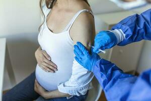 Enceinte vaccination. médecin donnant convoitise -19 coronavirus vaccin injection à Enceinte femme. médecin portant bleu gants vacciner Jeune Enceinte femme dans clinique. gens vaccination concept. photo