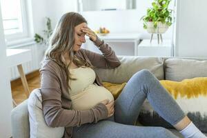 Enceinte Jeune adulte femme repos sur canapé à maison, sentiment indisposé. Jeune Enceinte femme a souffert de maux de tête séance sur le canapé. grossesse symptômes photo