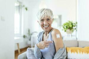 femme montrer du doigt à sa bras avec une bandage après recevoir le covid-19 vaccin. mature femme montrant sa épaule après avoir coronavirus vaccin photo