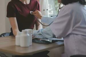 asiatique médecin femme a visité patient femme à diagnostic et vérifier en haut santé à Accueil ou privé hôpital. femelle patient Explique santé problème et symptômes à médecin .santé se soucier prime un service à Accueil photo