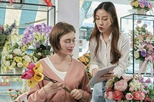 deux Jeune magnifique femelle fleuriste les partenaires discuter Floraison bouquet arrangement conception dans tablette, en ligne achat commande travail dans coloré fleur magasin boutique avec Frais flore, pme affaires entrepreneur. photo