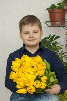 portrait de une jeune, magnifique garçon. détient une énorme brassée de Frais Jaune tulipes. le concept de printemps et vacances, Mars 8, international aux femmes jour, photo