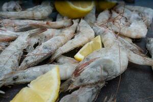 Frais et congelé crevette. Frais crevette est épars sur le table avec citron tranches. des produits pour grillage. citron tranches et congelé crevette. photo