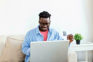 concept de technologie, de shopping, de banque, de maison et de style de vie - gros plan d'un homme avec un ordinateur portable et une carte de crédit à la maison. jeune homme utilisant des achats par carte de crédit en ligne. photo