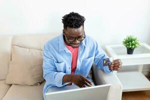 concept de technologie, de shopping, de banque, de maison et de style de vie - gros plan d'un homme avec un ordinateur portable et une carte de crédit à la maison. jeune homme utilisant des achats par carte de crédit en ligne. photo