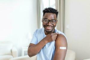 covid-19 vaccination. portrait de content vacciné africain homme montrant le sien bras après coronavirus antiviral vaccin coup . convoitise immunisation campagne concept. photo
