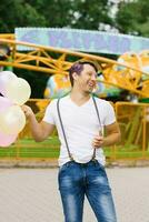 marrant gars détient une bouquet de des ballons dans le sien mains à un amusement parc et des rires photo